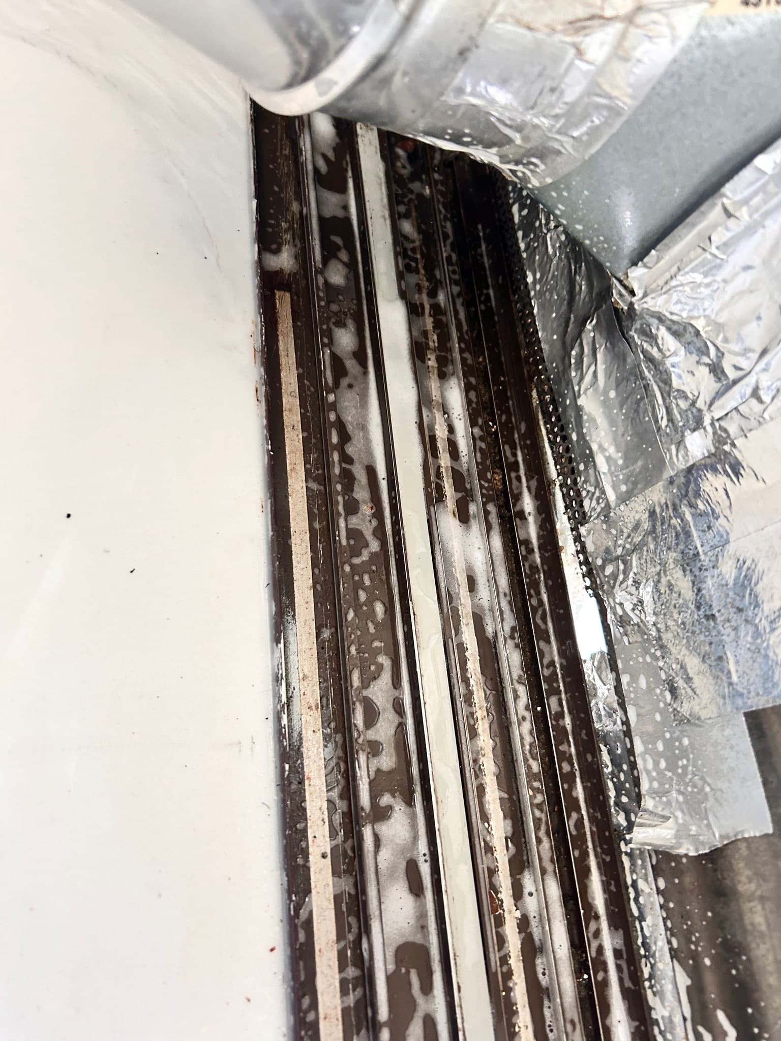 Sliding window track partway through a deep clean, with cleaning foam lifting grime out of the metal channels