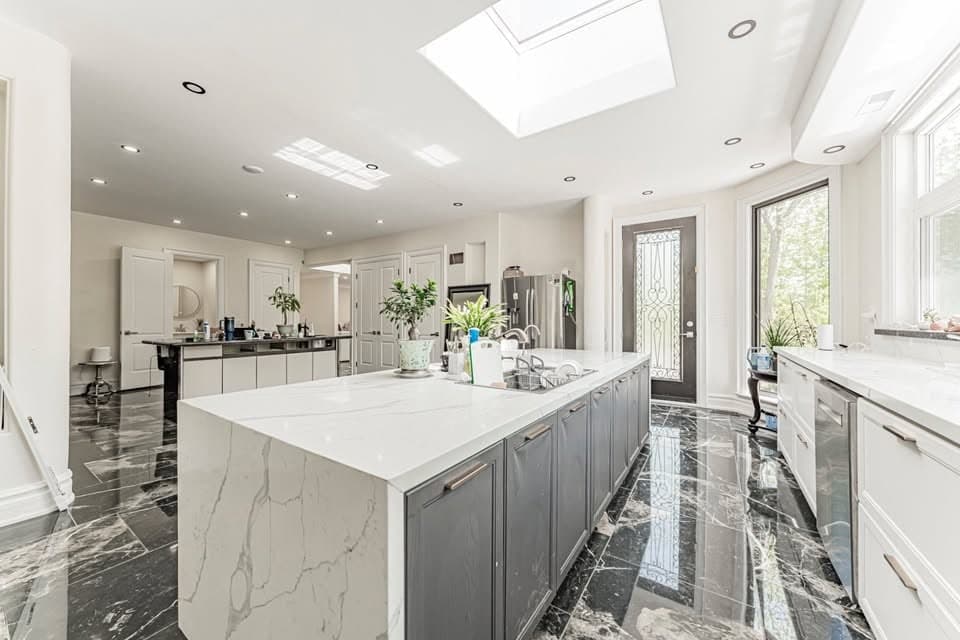 Large kitchen with a white waterfall-edge island, a skylight and a dark marble floor in a detached home